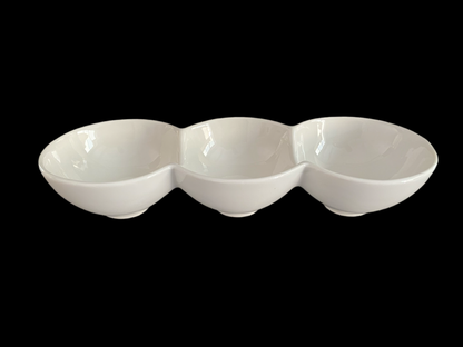 A white ceramic bowl with three compartments, each with a small amount of food inside, set against a black background.