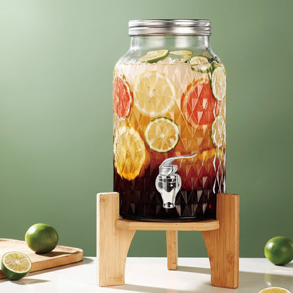 Glass drink dispenser with fruit slices on a wooden stand against a green background