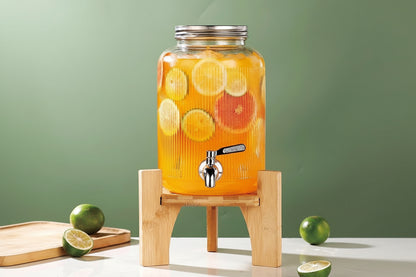 Juice dispenser with fruits on a wooden stand against a green background